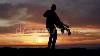 日落时分，父亲和女儿在海滩上玩耍的剪影。 暑假假期